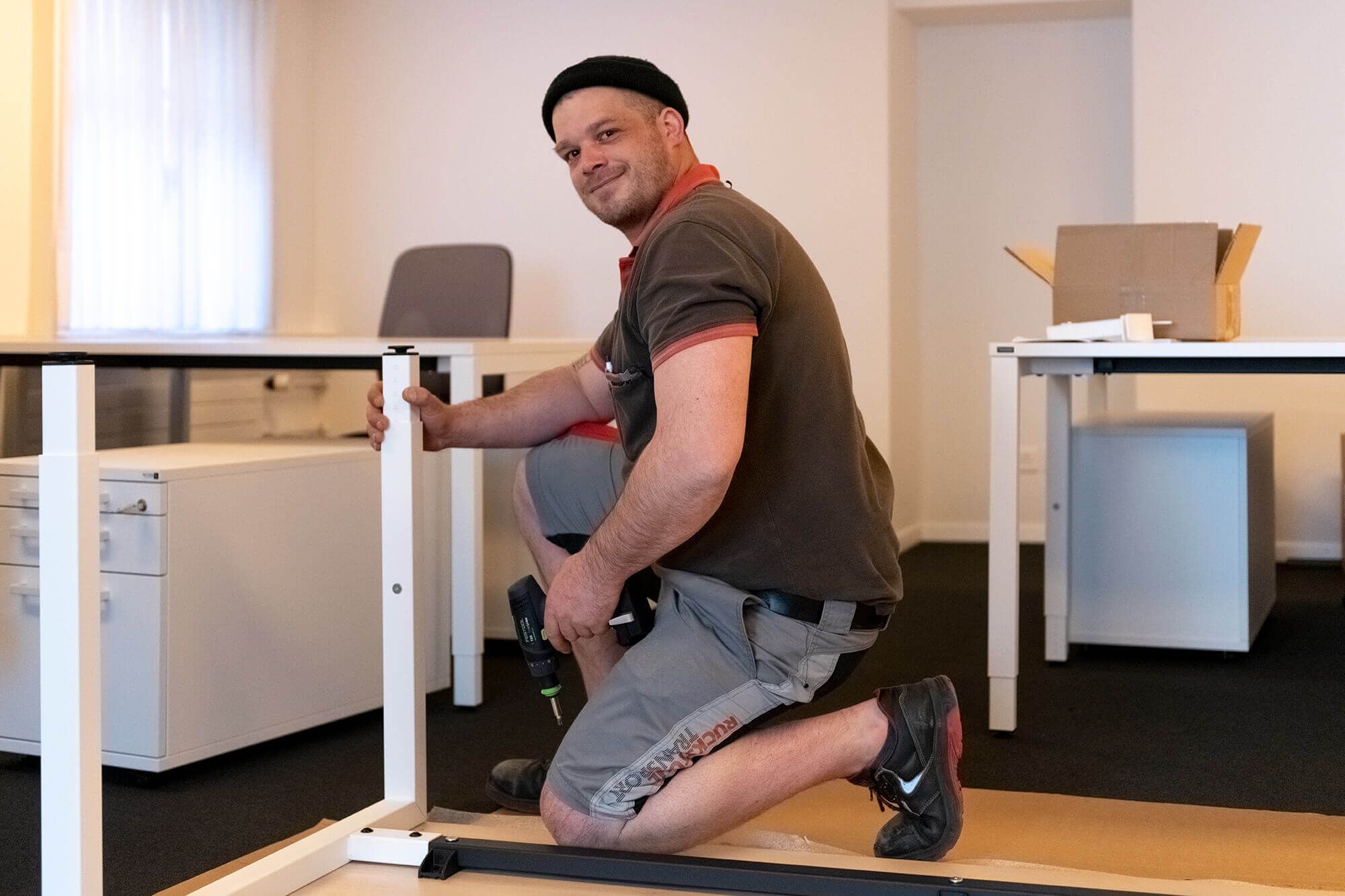 Glücklicher Ruckstuhl-Mitarbeiter montiert einen Tisch in einem Büro.